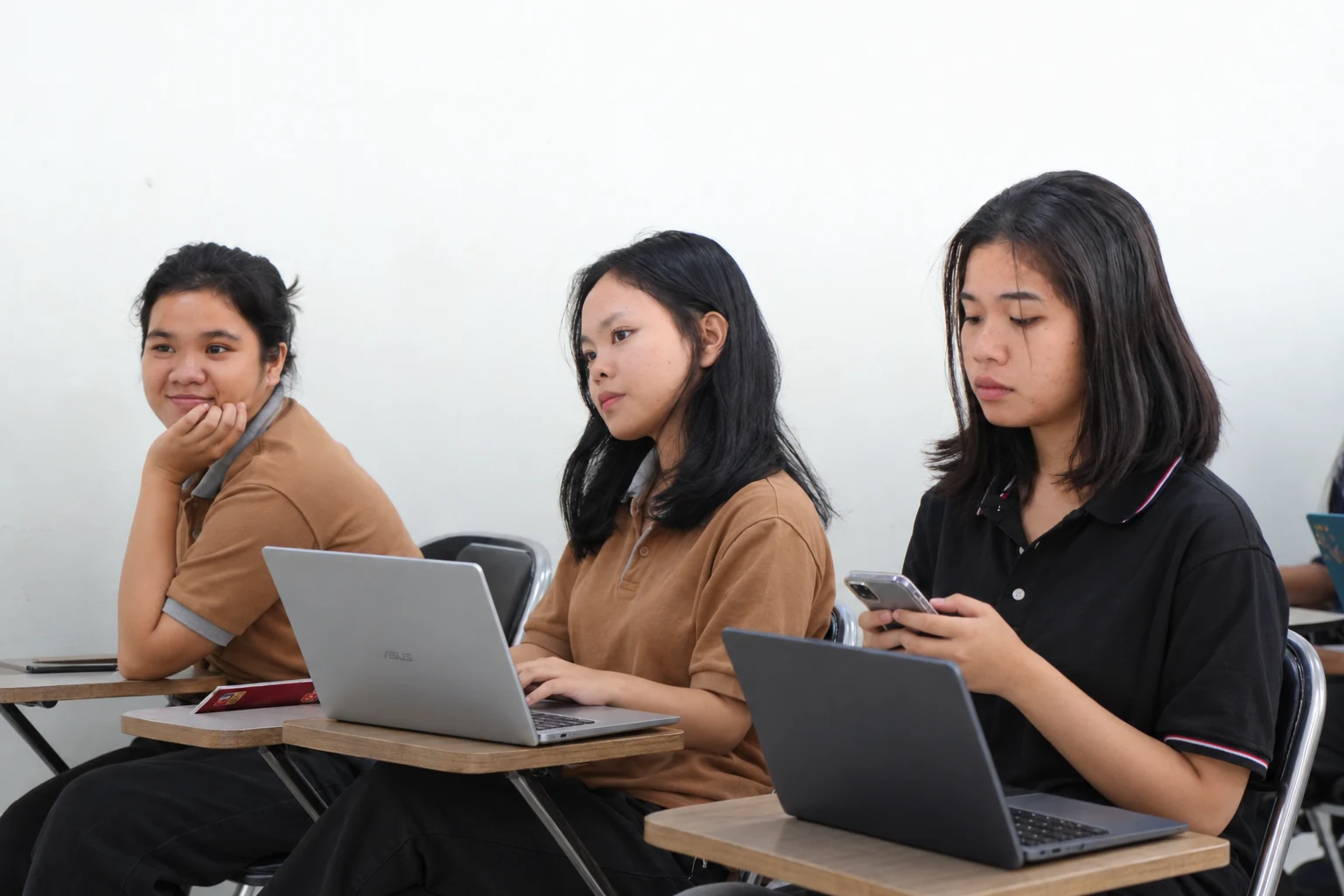 Mahasiswi menggunakan laptop dan ponsel untuk kegiatan akademik.